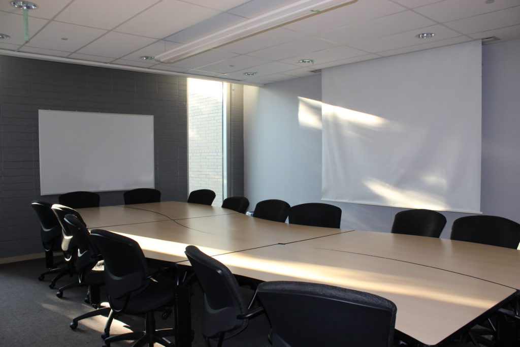 Image of a meeting room in MUSC with one long table with 15 chairs around